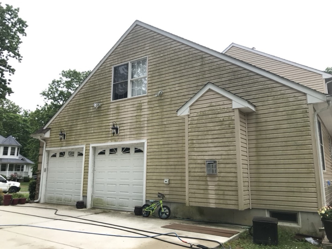 Garage and upper siding with visible organic buildup before exterior cleaning